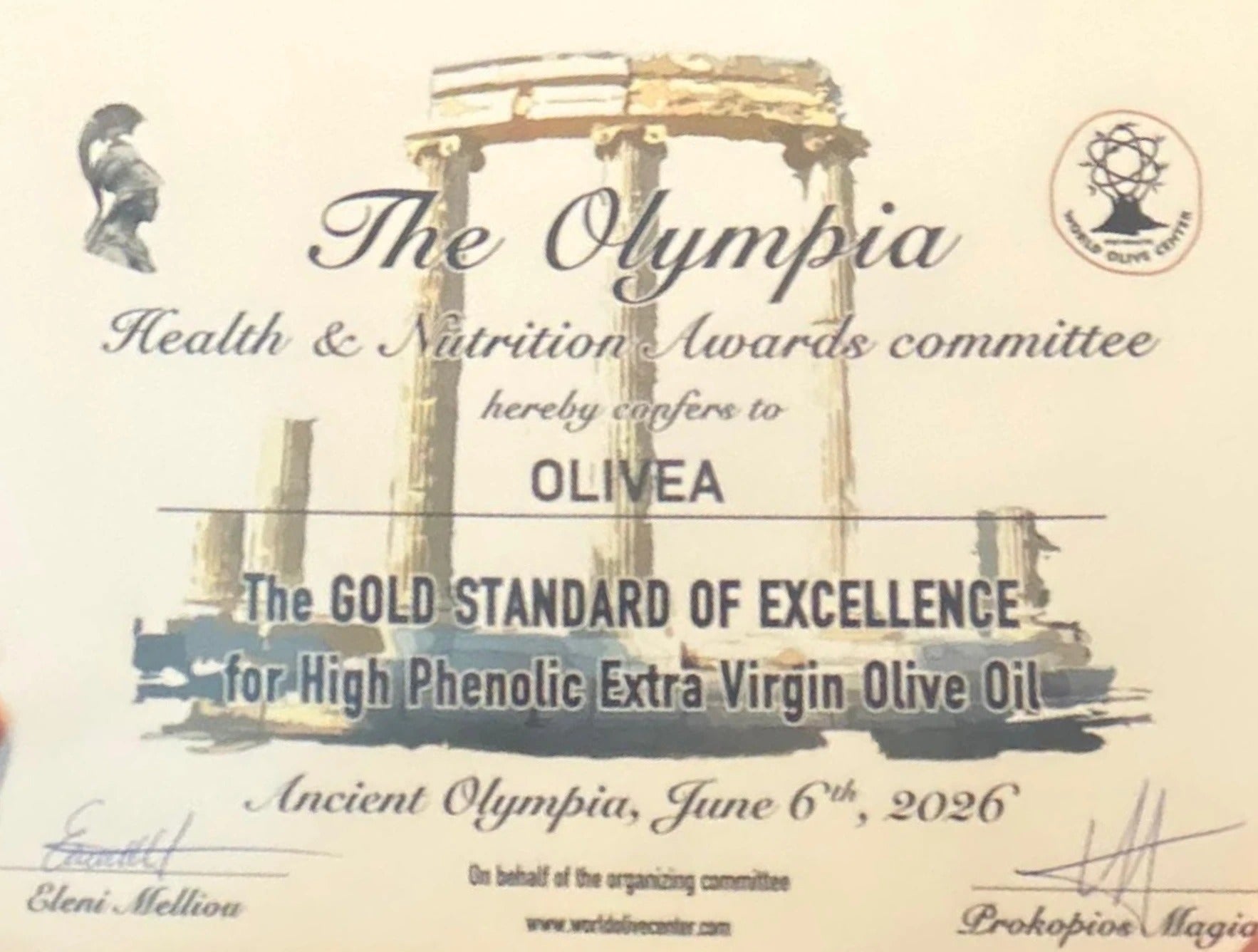 The 2026 Olympia Health & Nutrition Awards Gold Standard of Excellence certificate, awarded to Olivea for High Phenolic Extra Virgin Olive Oil. Signed by Dr. Eleni Melliou and Dr. Prokopios Magiatis at Ancient Olympia, Greece, June 6, 2026.